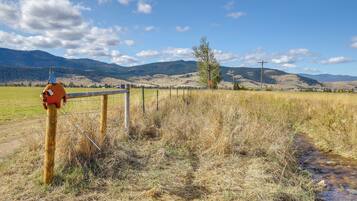 A rural landscape with a wooden fence, a metal gate, and a clear blue sky.