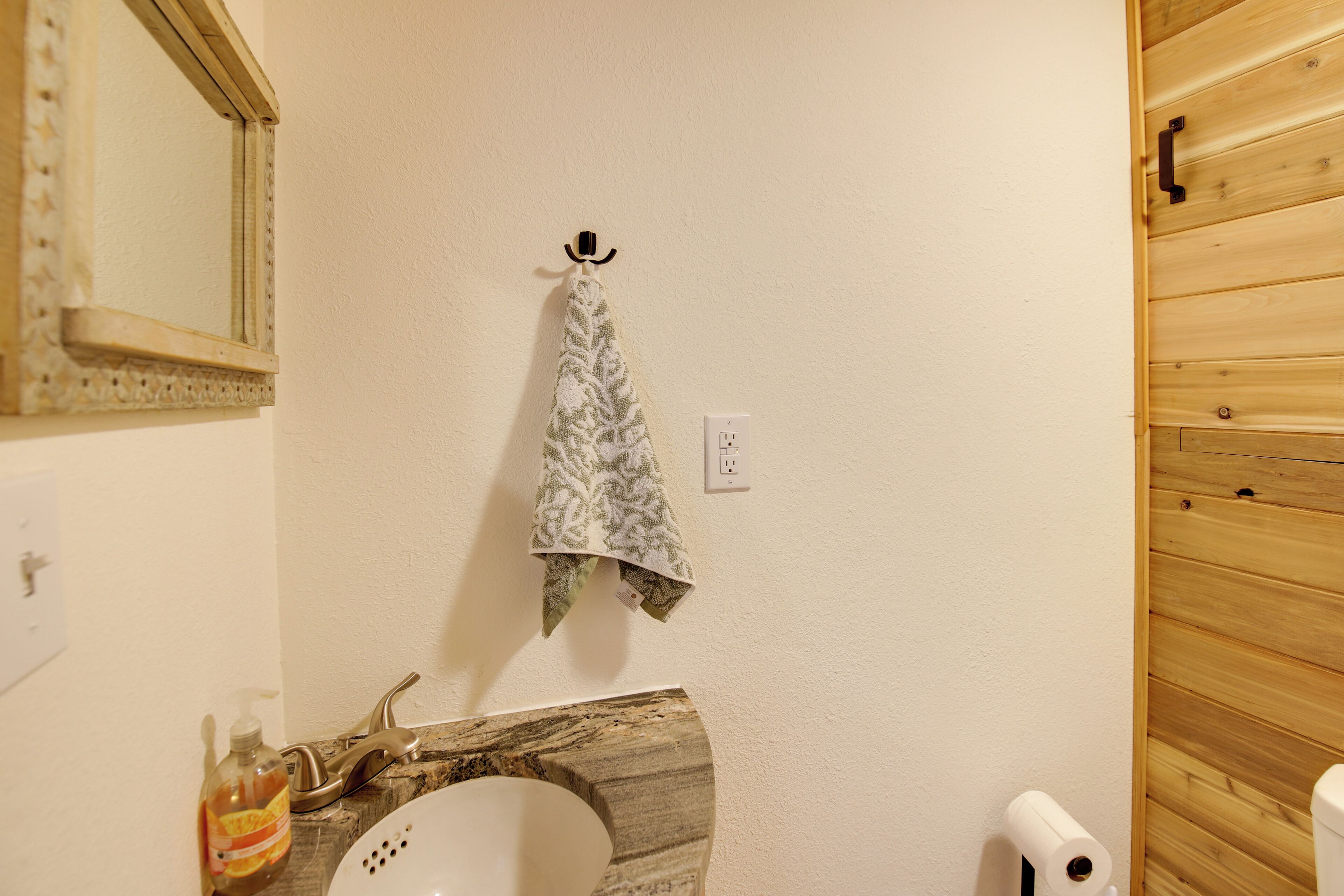 A bathroom with a wooden vanity, a towel hanging on a hook, a soap dispenser, and a toilet paper holder.
