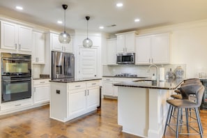A modern kitchen with white cabinetry, stainless steel appliances, and a central island with bar stools.