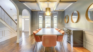 Een ruime eethoek met een lange tafel, meerdere stoelen en een trap naar een andere kamer.