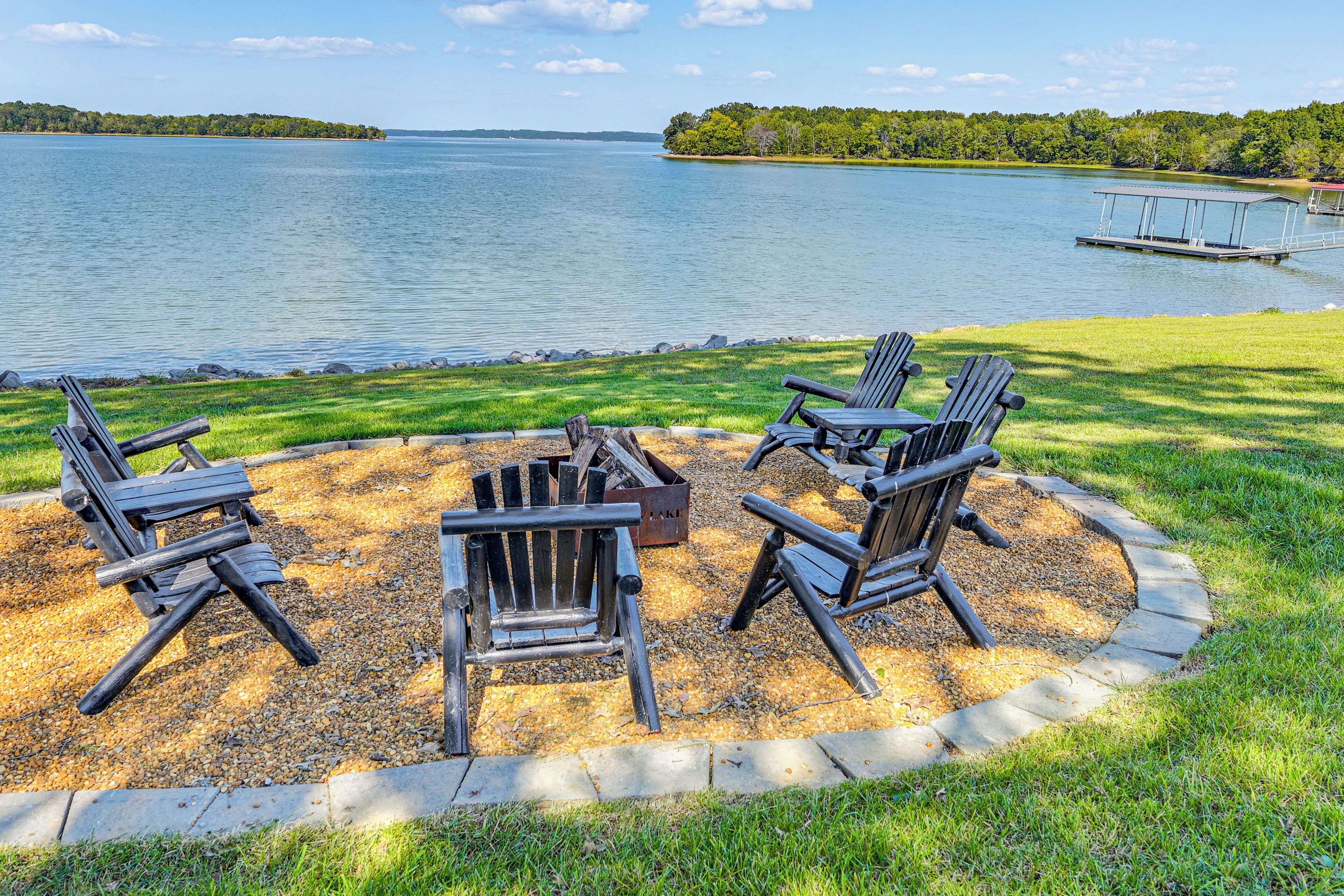 A lakeside seating area with Adirondack chairs and a fire pit.