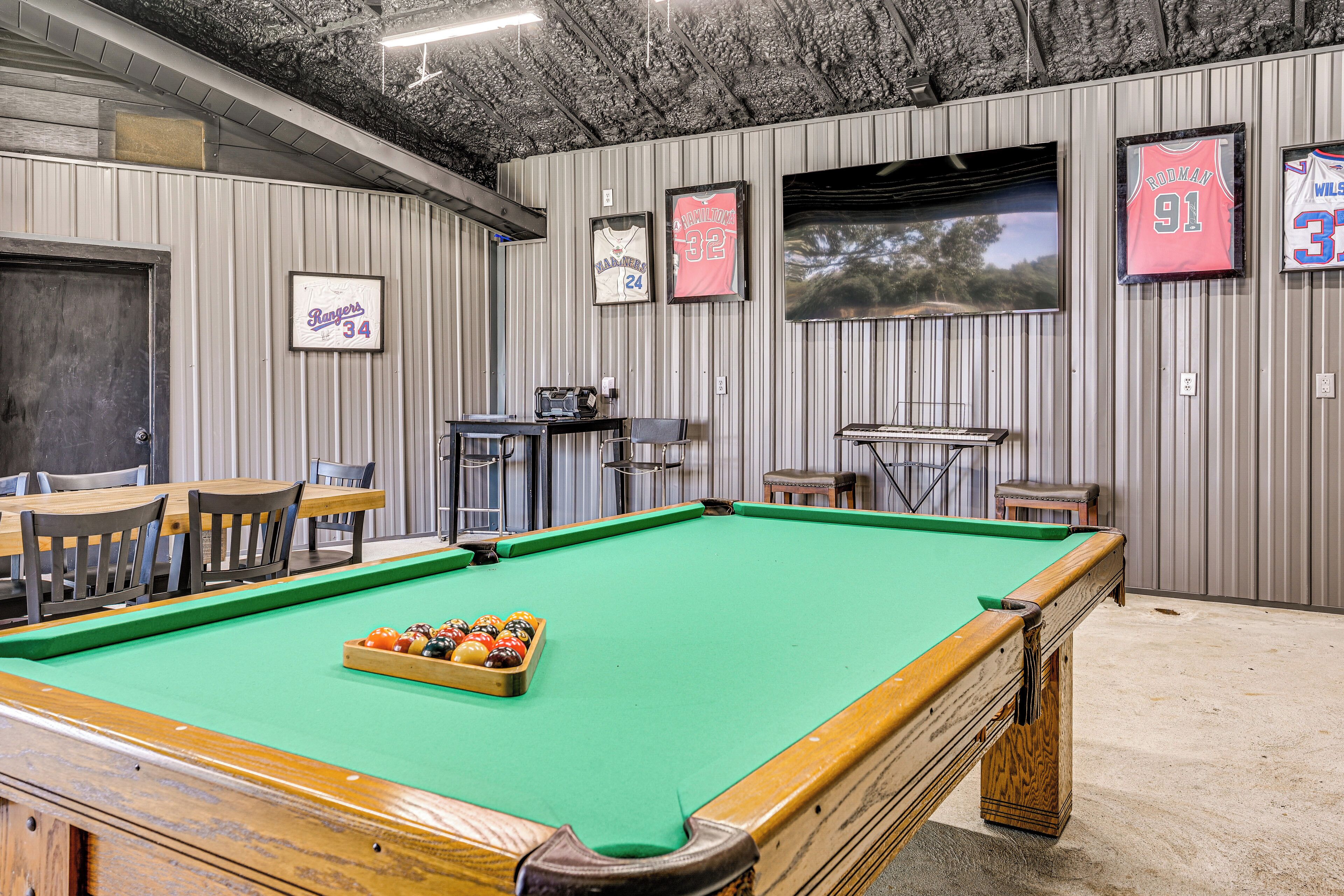 Une table de billard recouverte d’un drap vert, entourée de chaises et d’une table avec un coin bar.