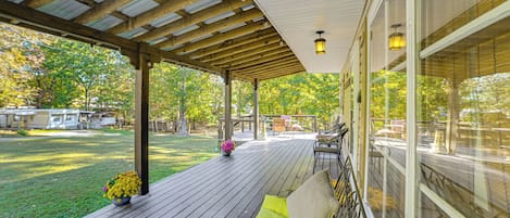 A covered deck with a wooden floor, a cushioned bench, and a flower pot.