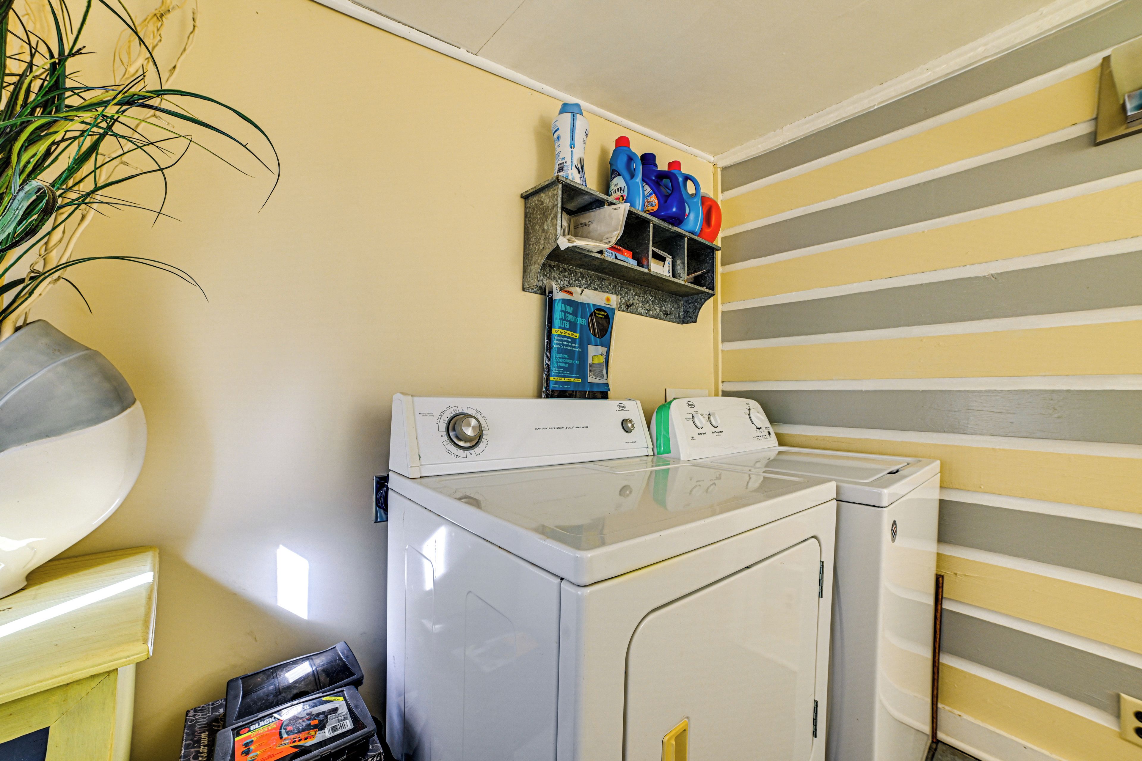 A laundry area with a washing machine, a shelf with detergent bottles, and a potted plant.