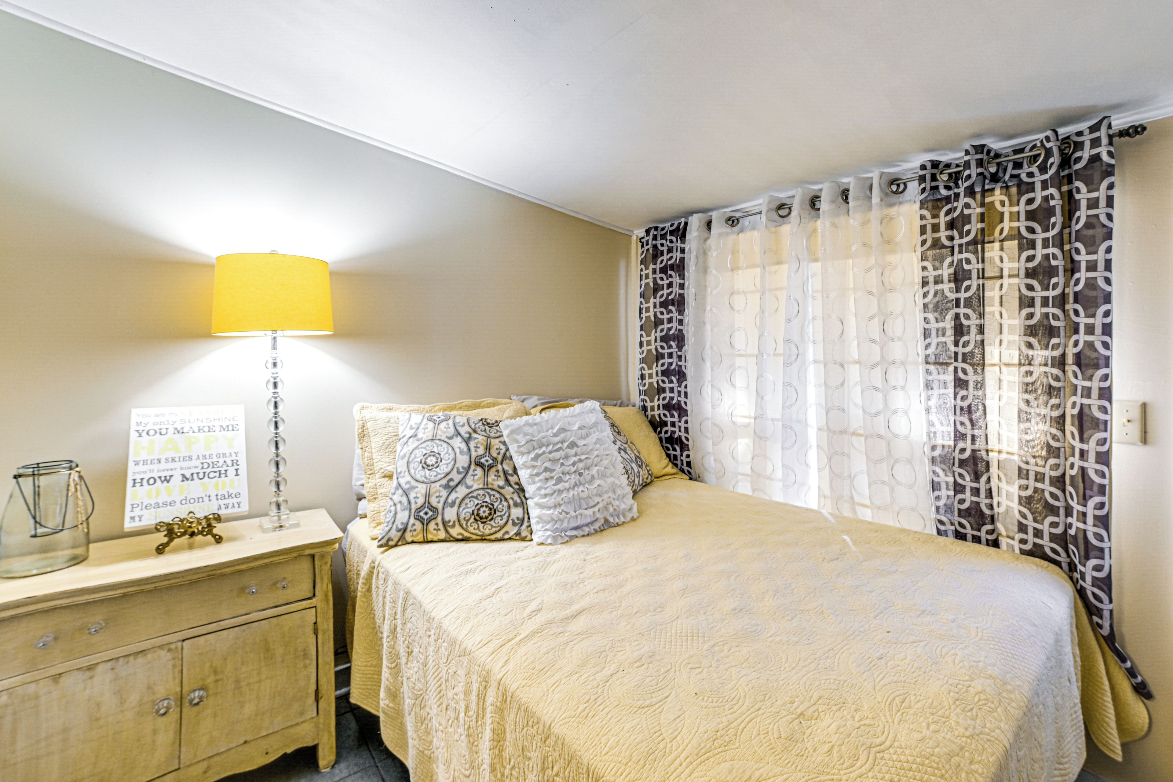 A neatly arranged bedroom with a bed, bedside table, lamp, and a decorative sign.