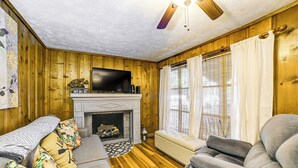 A cozy living room with a fireplace, wooden walls, a sofa, and a television. - < 1 Mi to Fishing: Springville Home w/ Fireplace! (Springville)