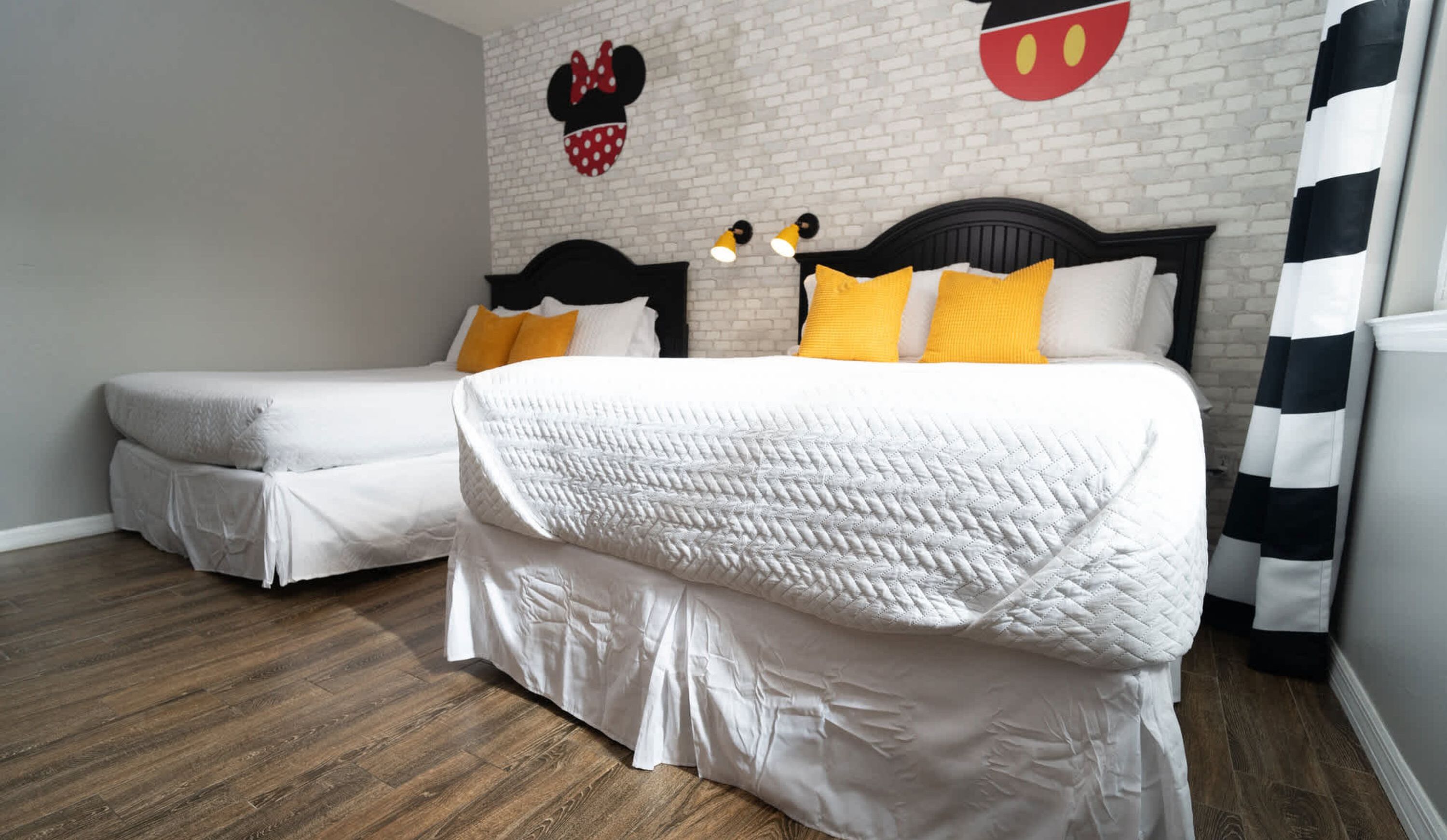 A hotel room with two beds, a brick wall, and Mickey Mouse decorations.