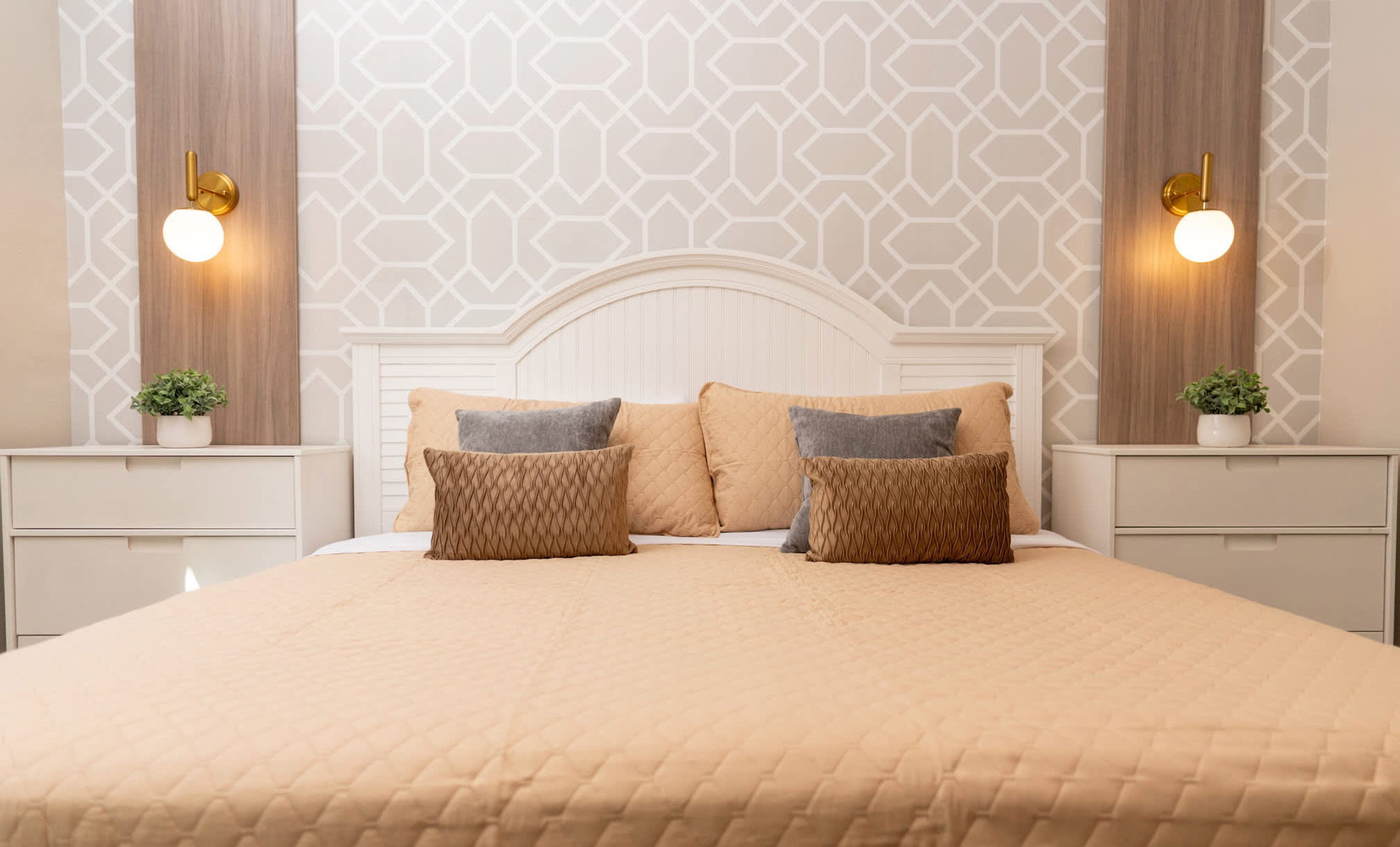 A neatly made bed with a quilted cover, two bedside tables with lamps, and a geometric patterned wall.