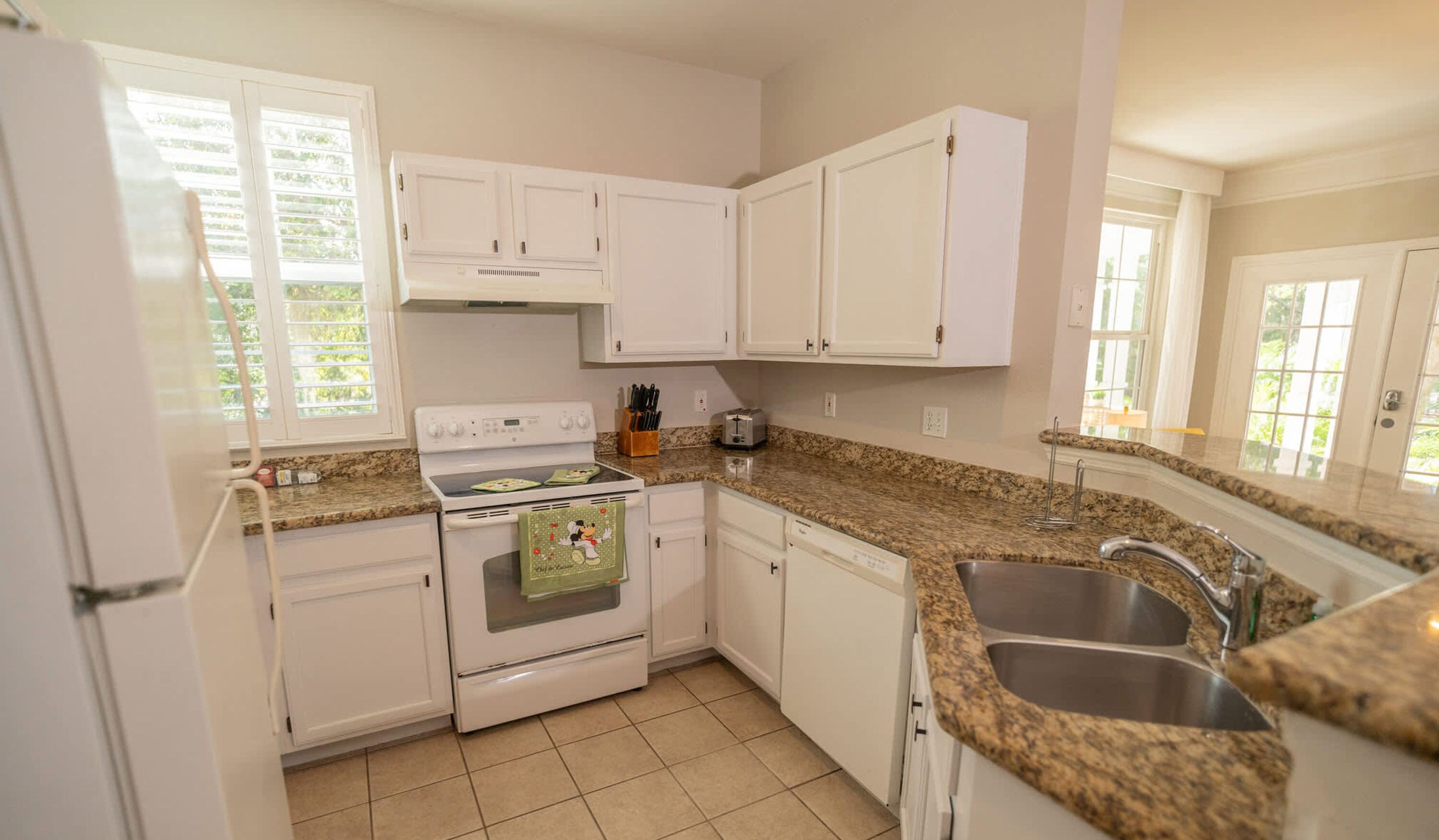 A kitchen with white cabinets, a granite countertop, a stainless steel sink, and a window with blinds.
