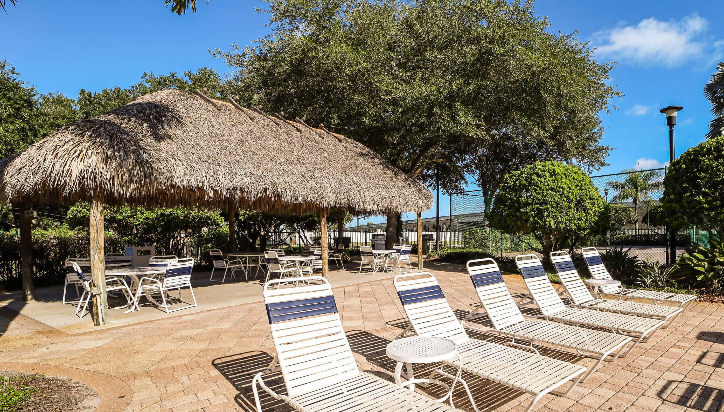 A sunlit outdoor seating area with thatched umbrellas, lounge chairs, and tables.