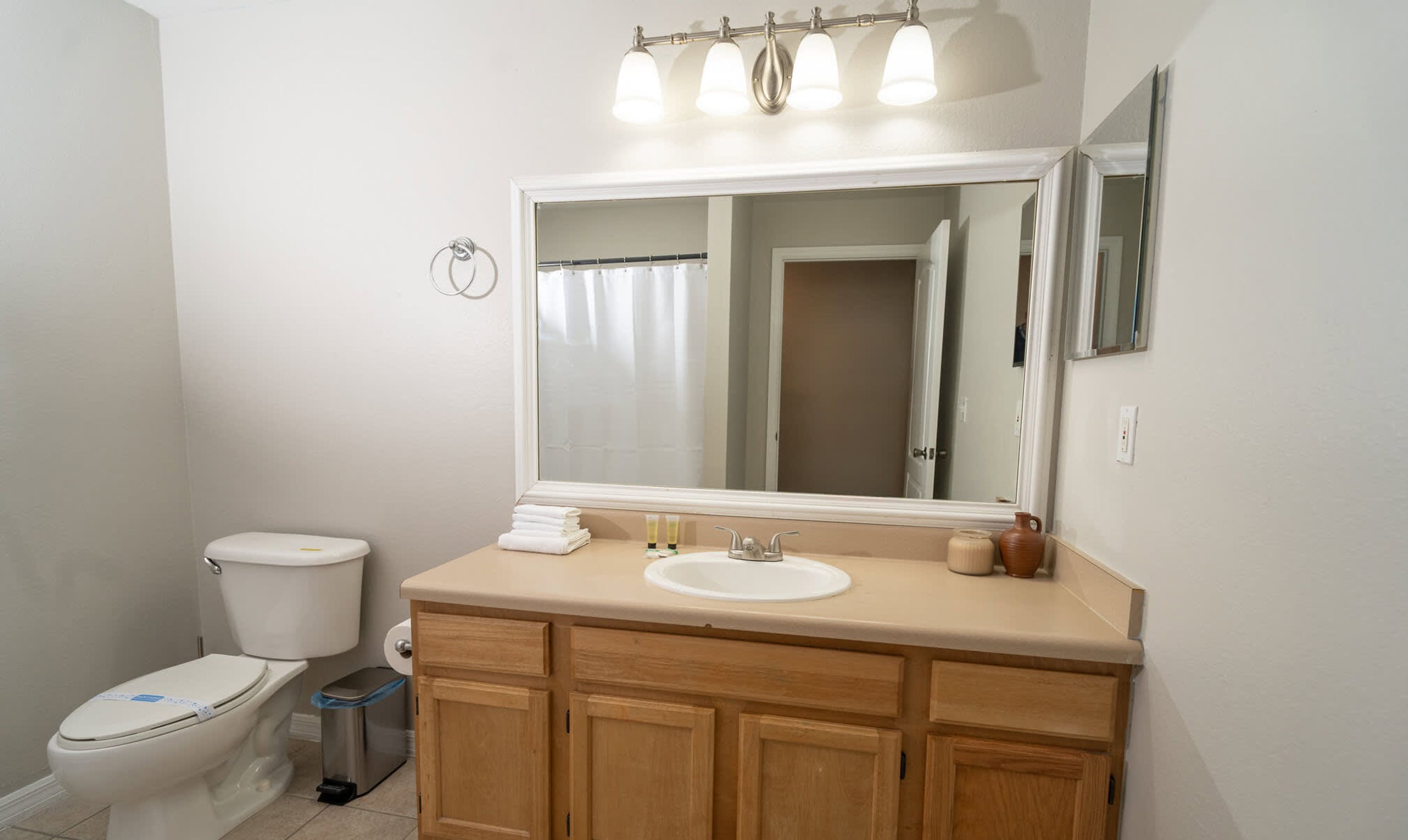 A bathroom with a toilet, sink, vanity, and a large mirror.