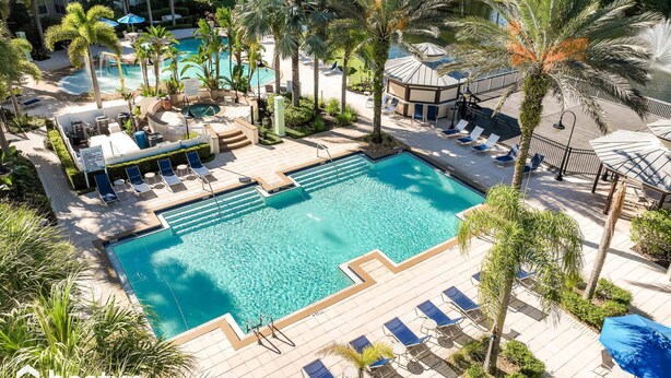 A resort pool area with multiple lounge chairs, palm trees, and a clear blue pool. - Magical Themed 3BR Townhouse Near the Parks (Kissimmee)