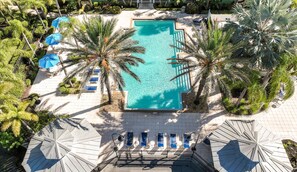 An aerial view of a resort pool area with a rectangular pool, surrounded by palm trees and sun loungers. - Magical Themed 3BR Townhouse Near the Parks (Kissimmee)