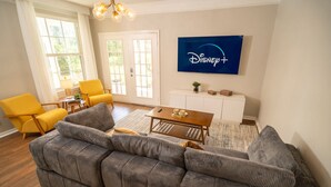 A living room with a sofa set, a coffee table, and a TV mounted on the wall displaying the Disney+ logo. - Magical Themed 3BR Townhouse Near the Parks (Kissimmee)