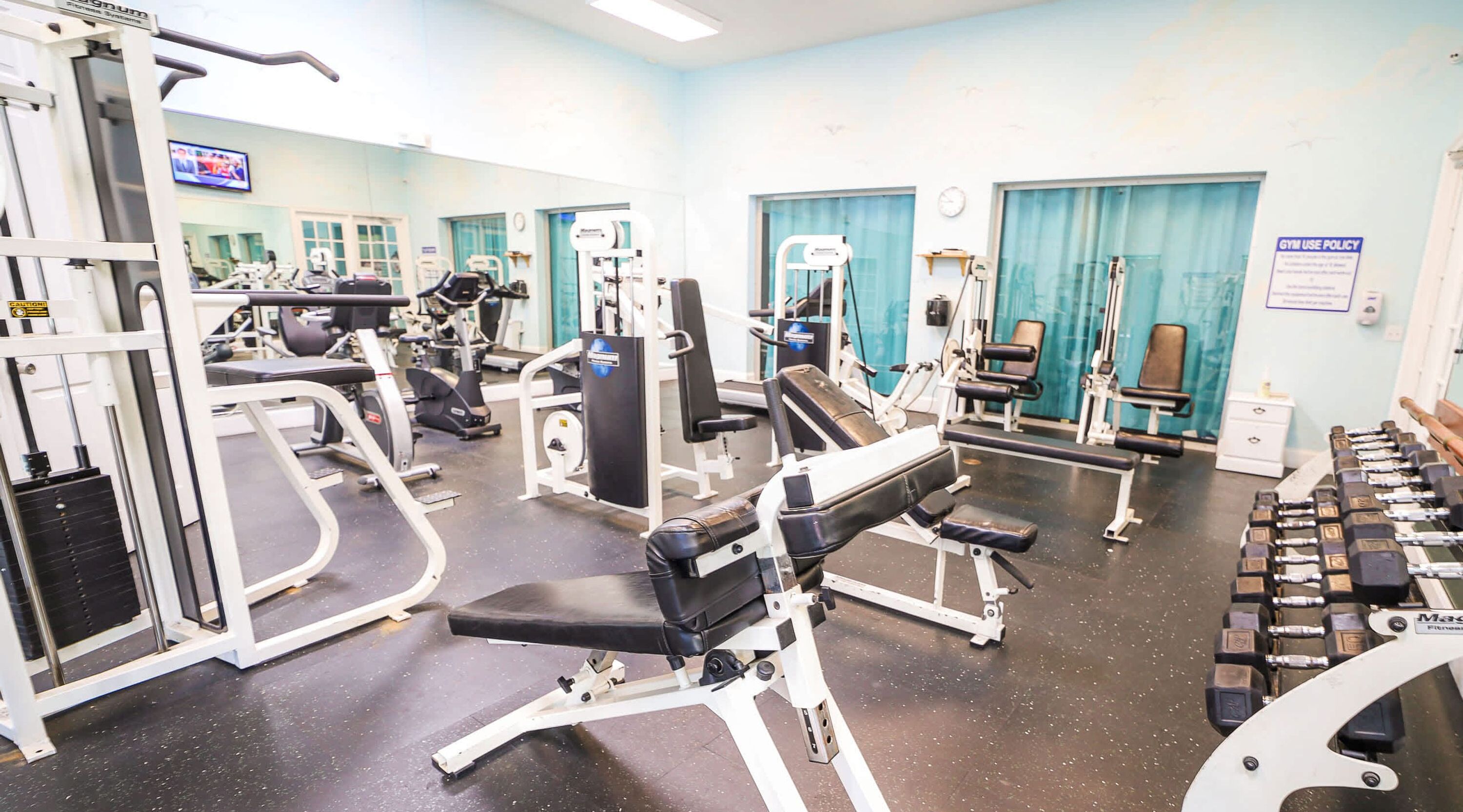 A gym with various exercise equipment, including weight machines, benches, and dumbbells.