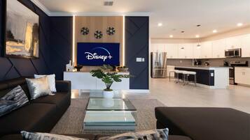 A modern living room with a dark-colored sofa, a glass coffee table, and a flat-screen TV displaying the Disney+ logo.