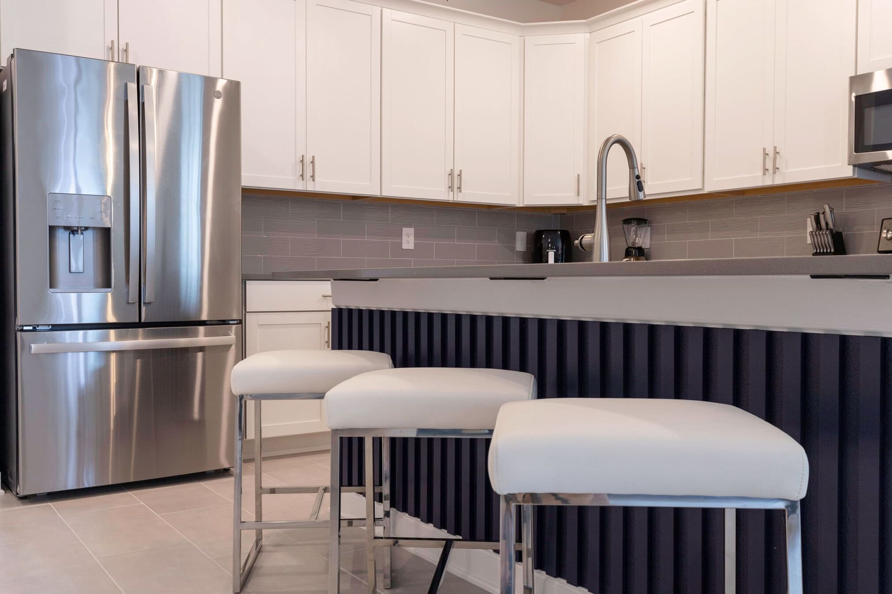Una cocina moderna con electrodomésticos de acero inoxidable, armarios blancos, una encimera gris y un salpicadero negro.