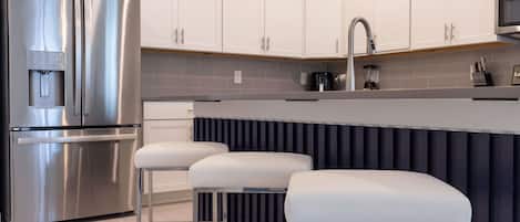 Una cocina moderna con electrodomésticos de acero inoxidable, armarios blancos, una encimera gris y un salpicadero negro.