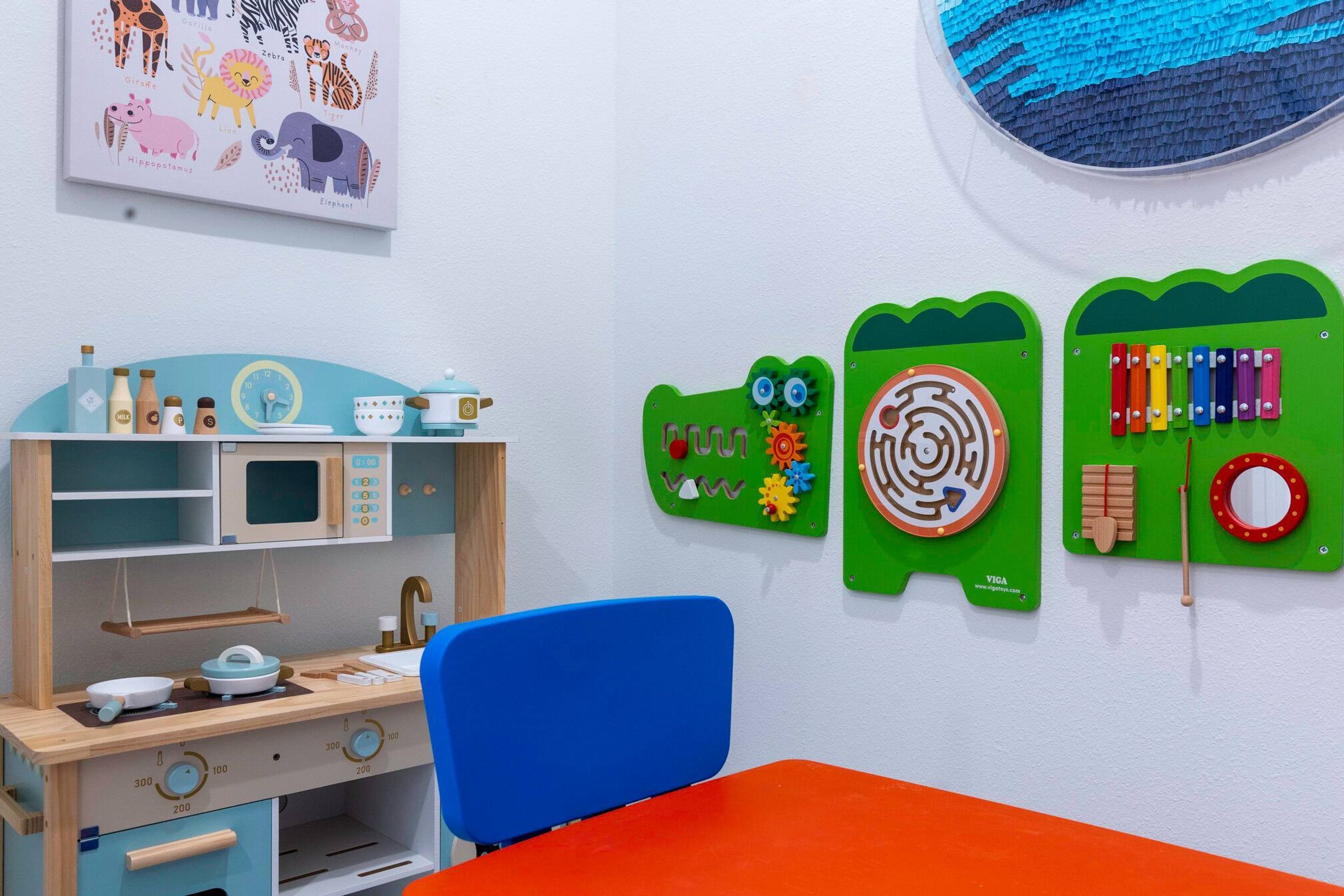 Un espace de jeux pour enfants avec un bureau en bois, une chaise bleue et des décorations murales à caractère éducatif.