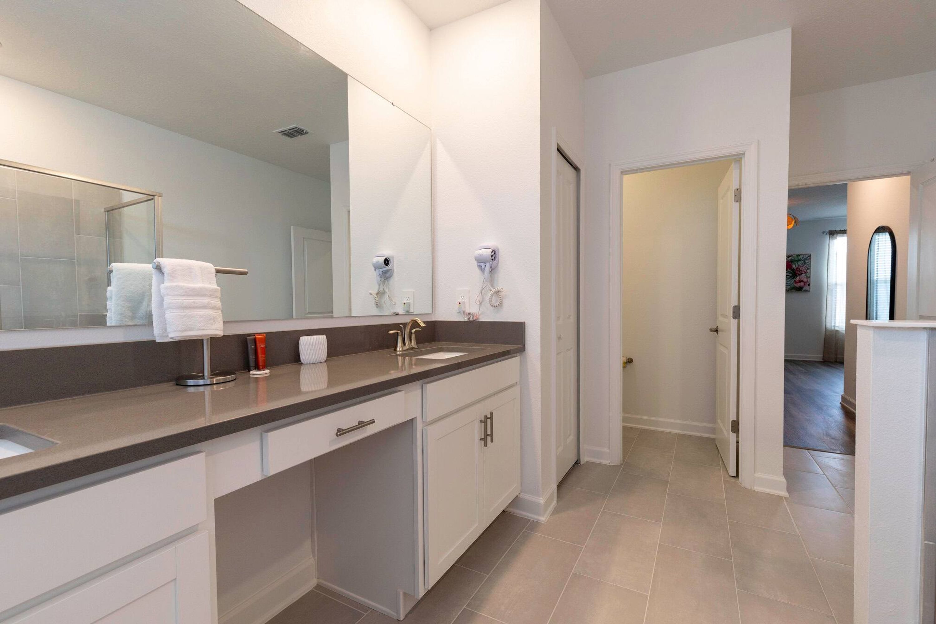 A modern bathroom with a large mirror, two hair dryers, a sink, and a toilet.