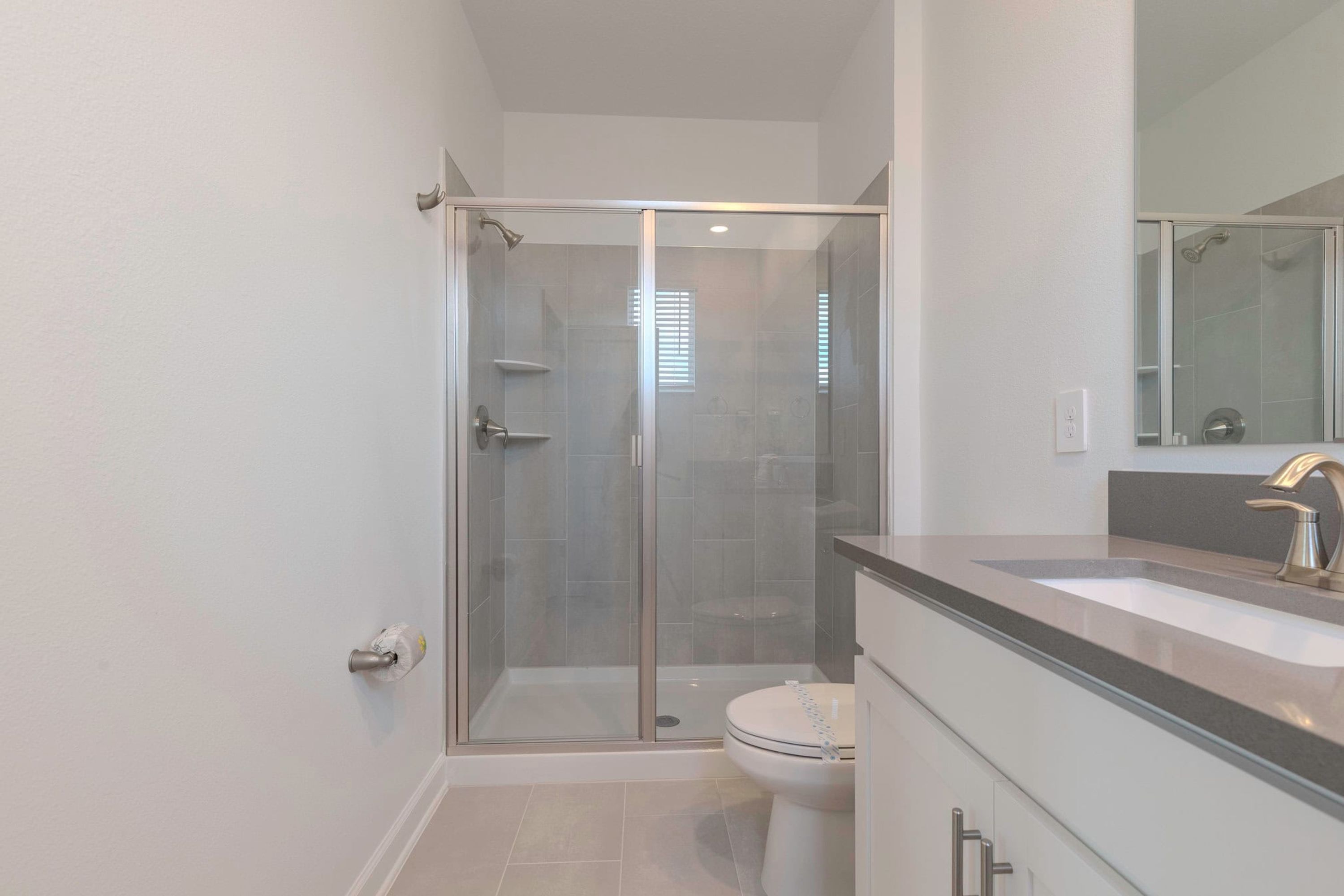 A modern bathroom with a glass-enclosed shower, a toilet, and a vanity with a sink and mirror.