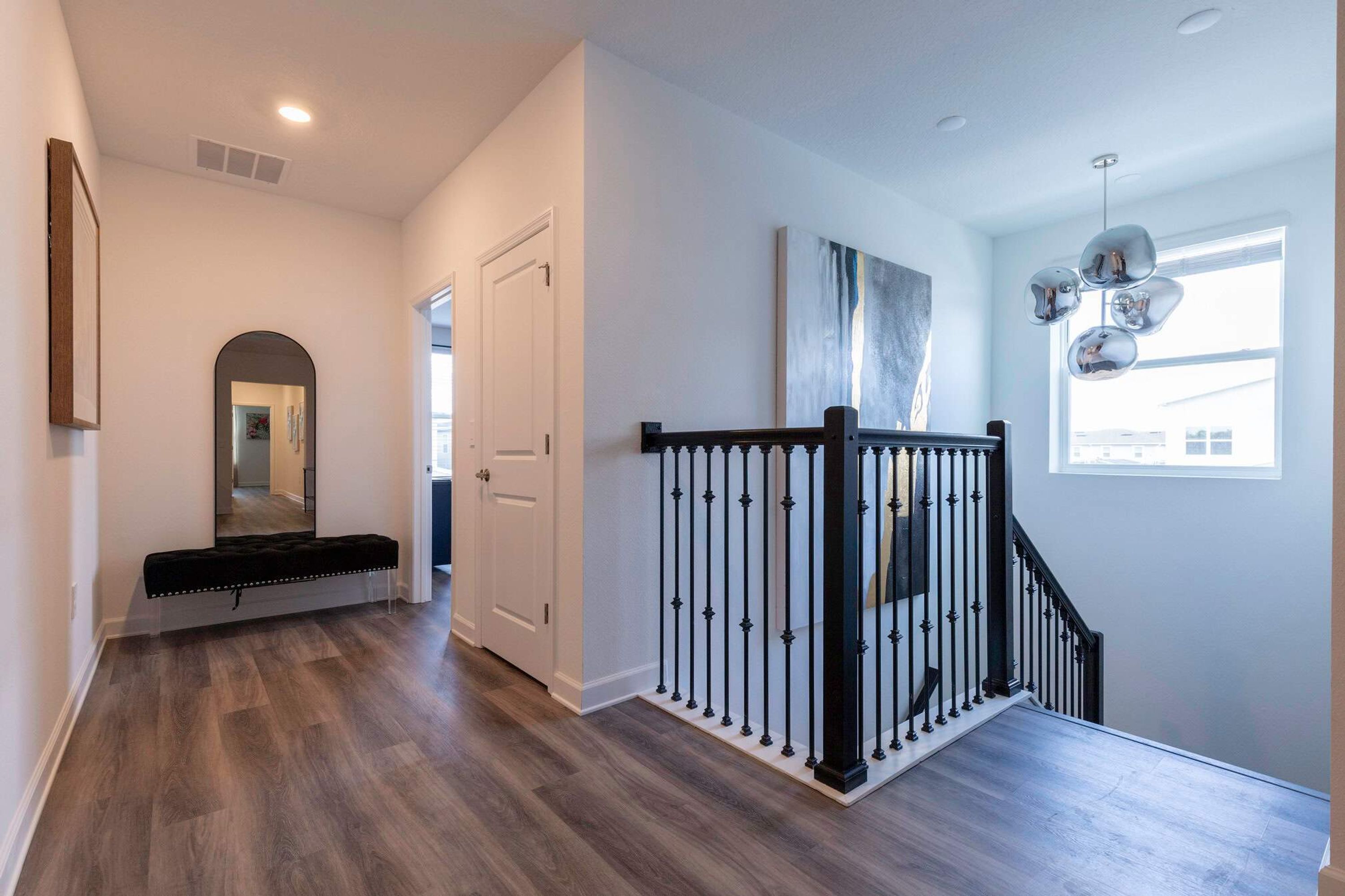 A modern interior with a wooden floor, a staircase with black railings, a bench, and a large mirror.