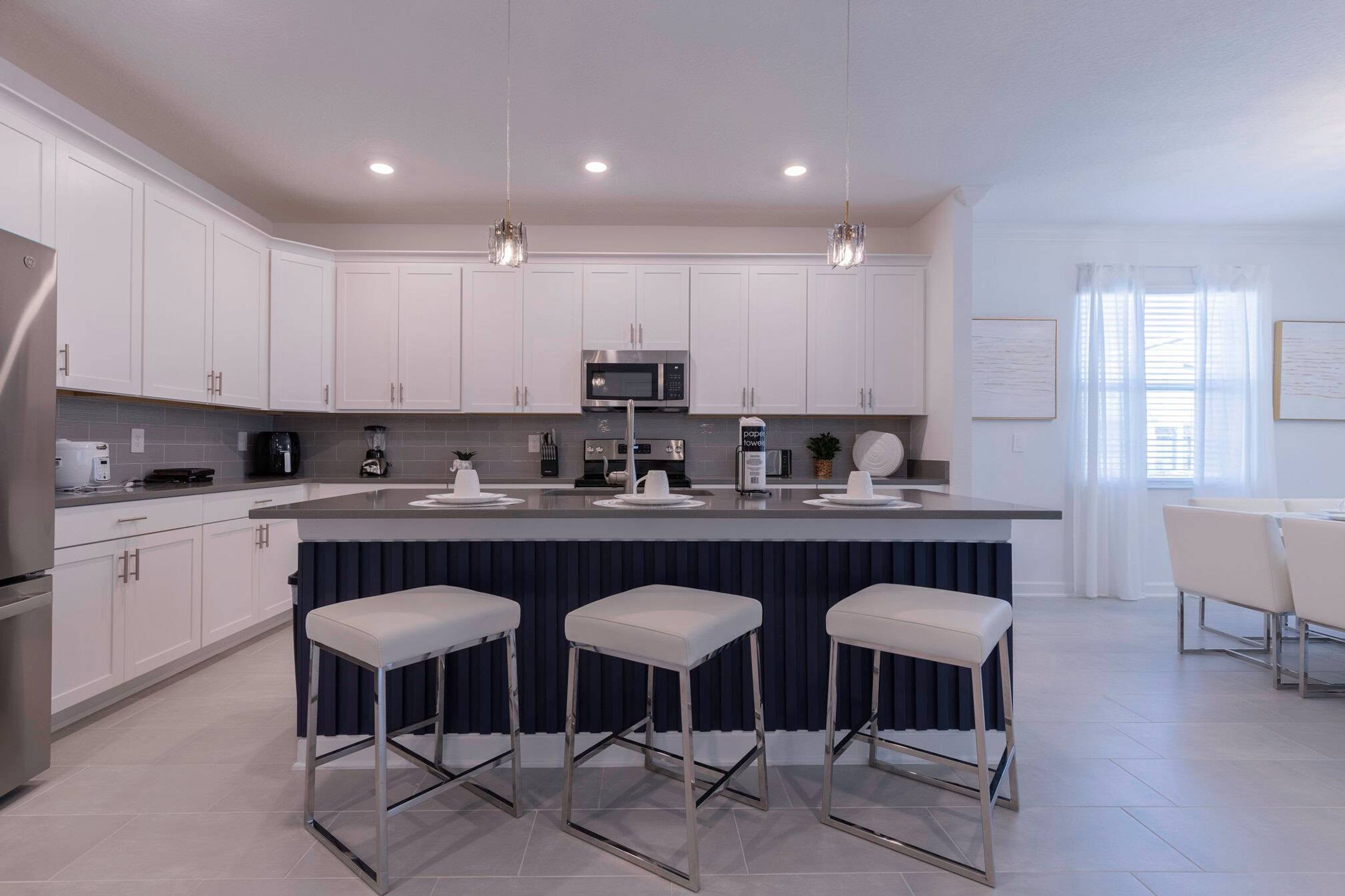A modern kitchen with white cabinets, stainless steel appliances, and a central island with bar stools.
