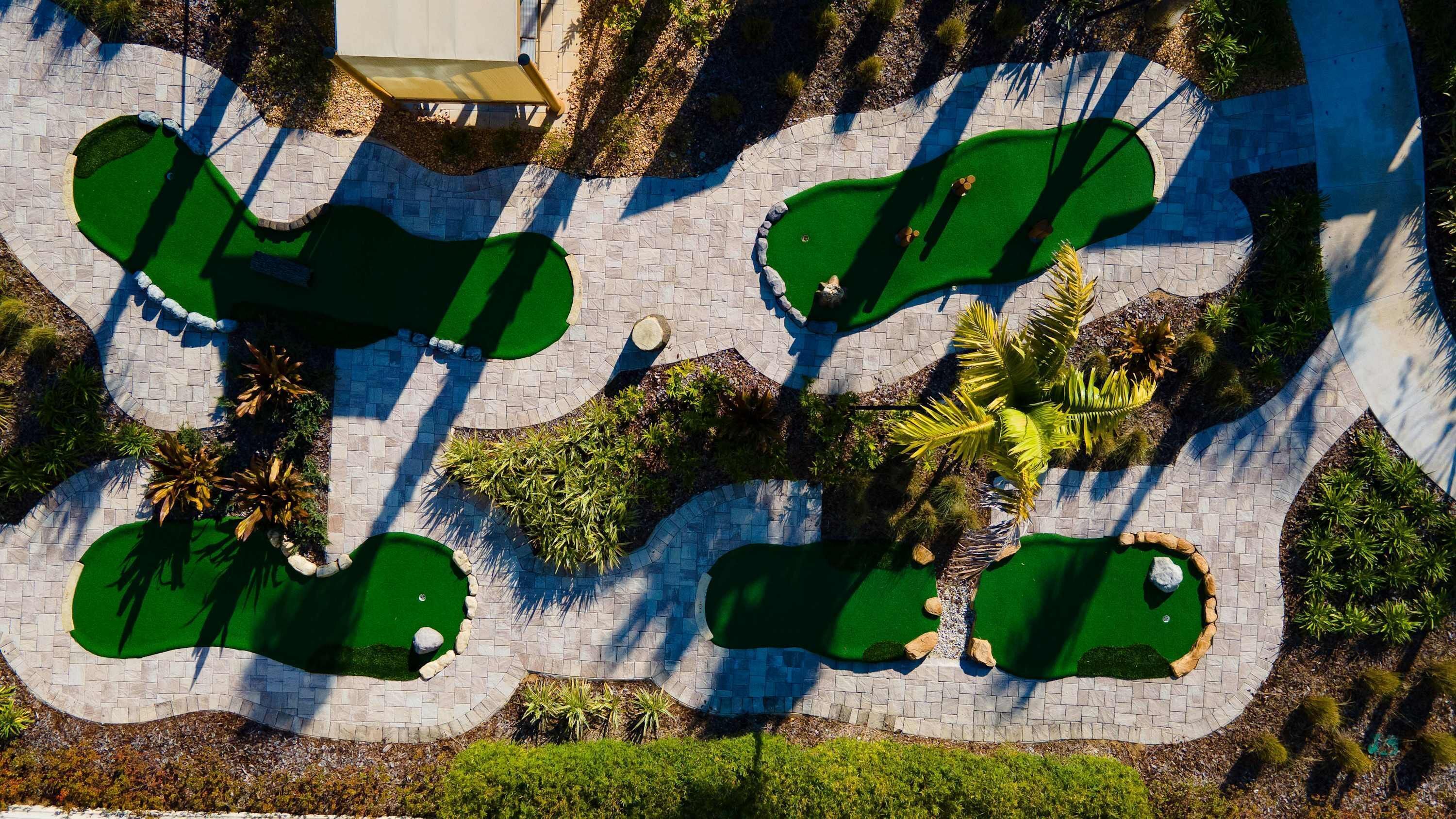An aerial view of a golf course with multiple green areas, pathways, and surrounding landscaping.