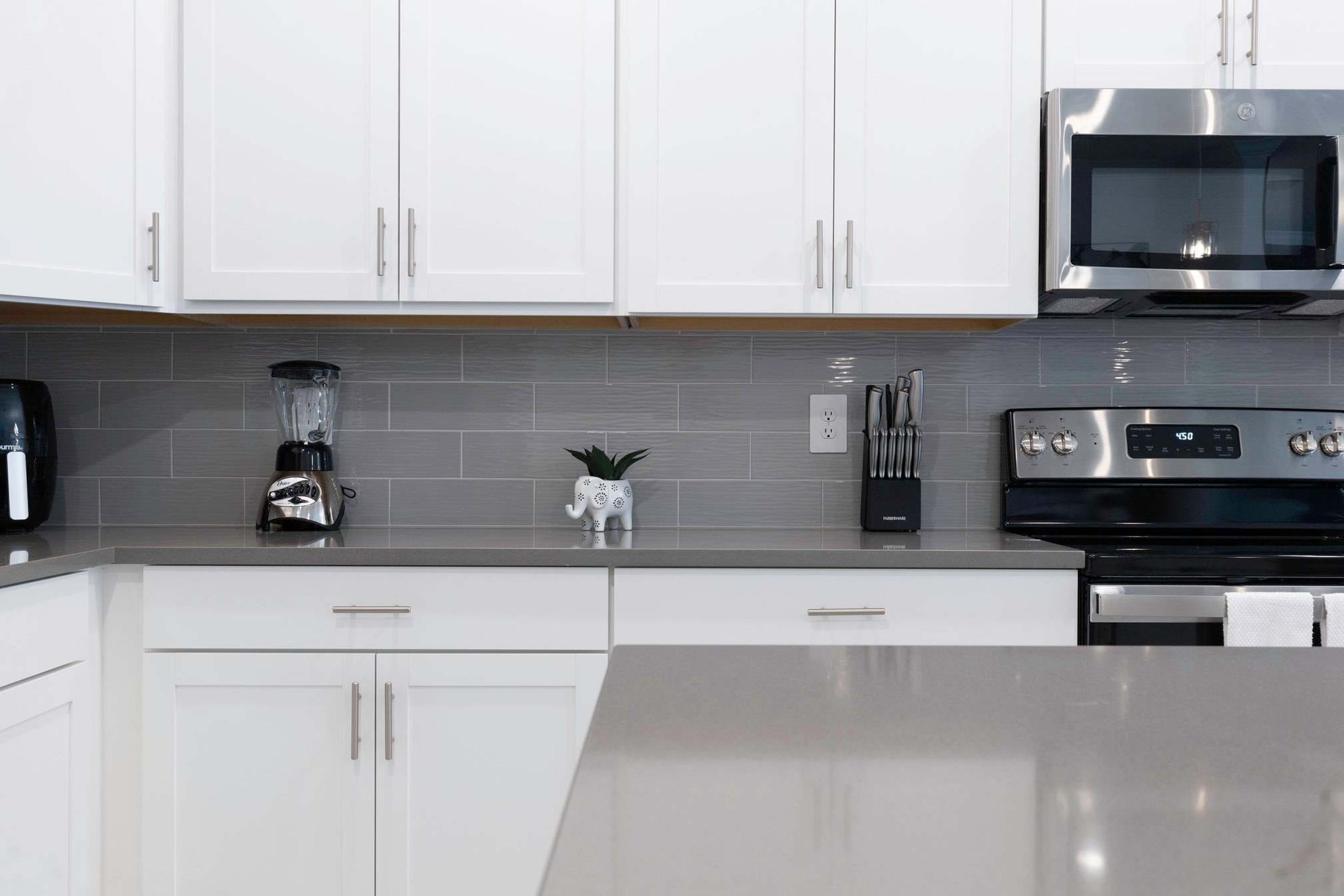 A modern kitchen with white cabinets, a built-in microwave, a stove, and a blender on the countertop.