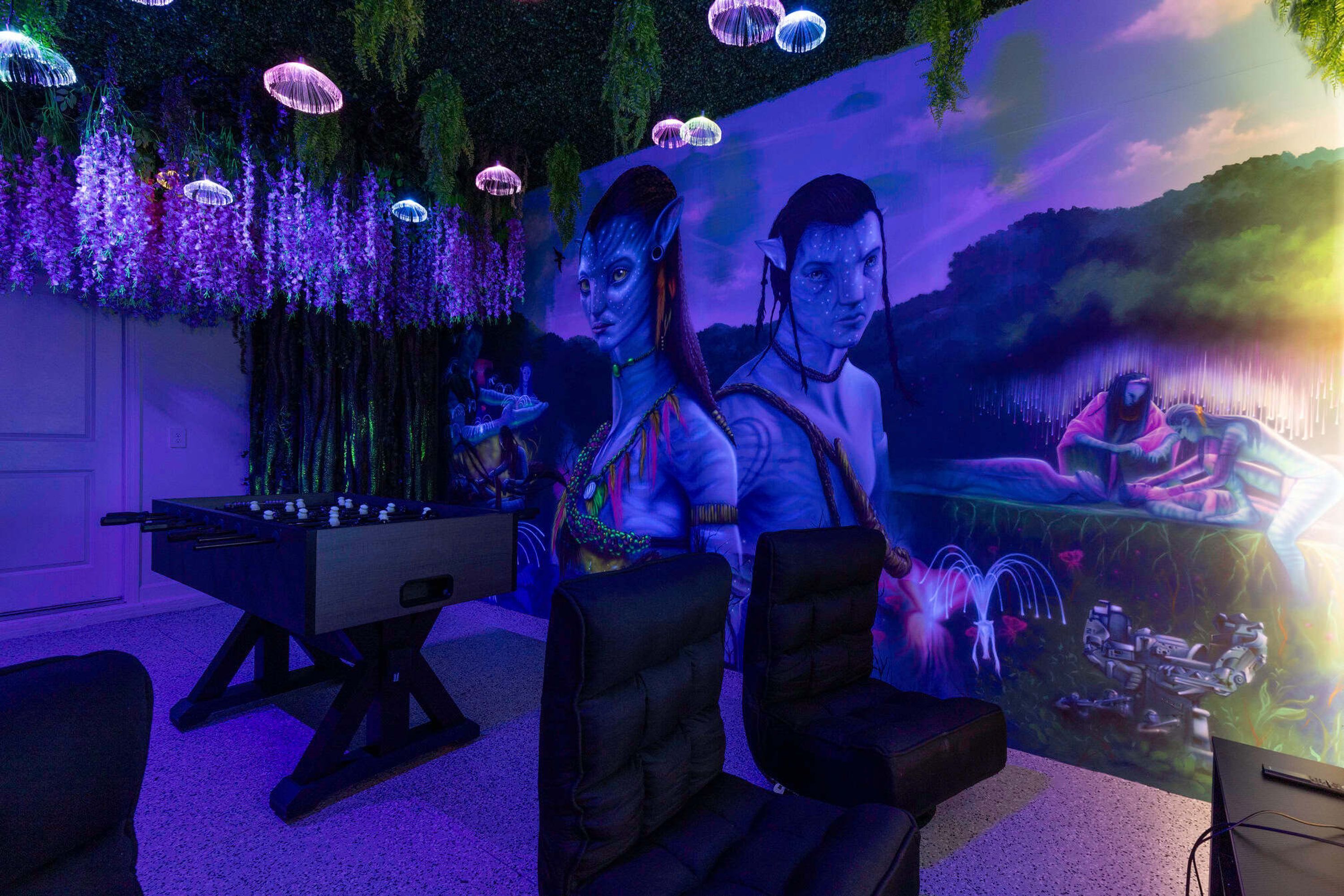 A room with a foosball table, plush seating, and a mural with a waterfall and fantasy elements.