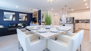 A modern dining area with a white table set for six, surrounded by white chairs. There is a large potted plant in the center. - Luxury 6BR Villa w Pool Jacuzzi Fun in Orlando (Kissimmee)