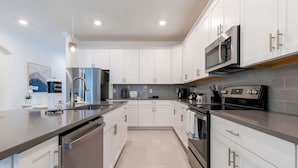 A modern kitchen with white cabinets, stainless steel appliances, and a grey countertop. - Luxury 6BR Villa w Pool Jacuzzi Fun in Orlando (Kissimmee)