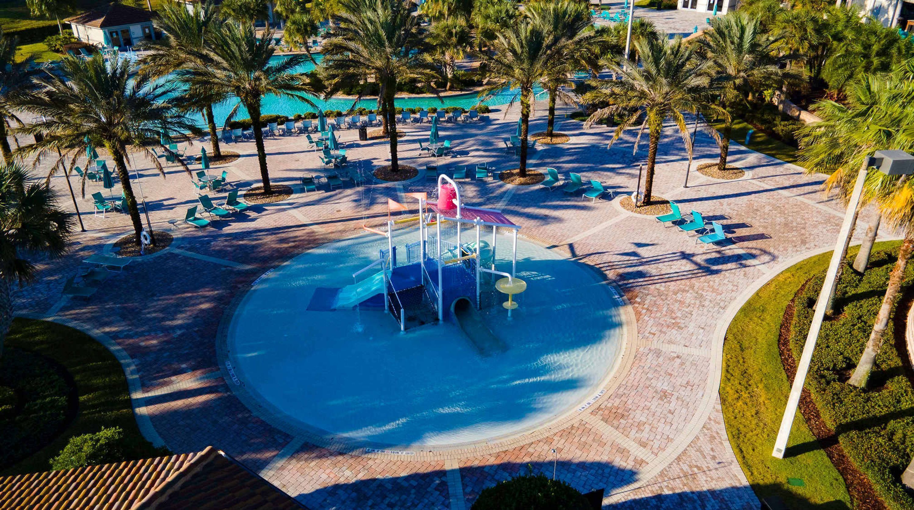 Un parc aquatique doté d’une structure de jeux centrale, entourée de palmiers et de chaises longues.