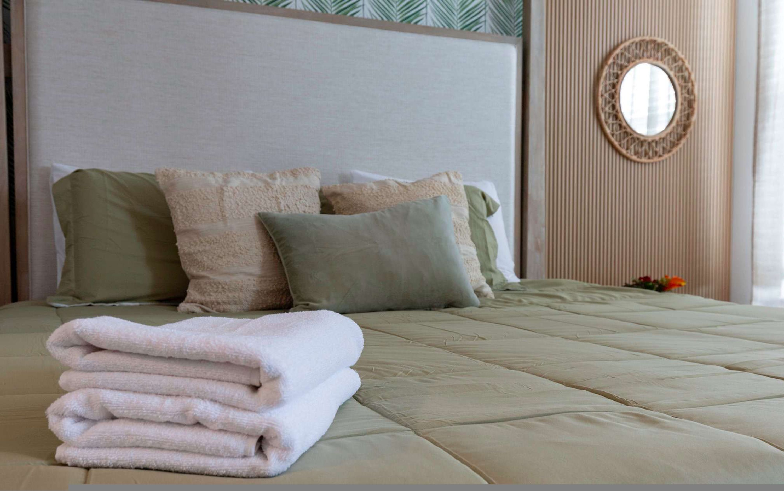A neatly made bed with a folded white towel on the side, a headboard, and a decorative mirror on the wall.