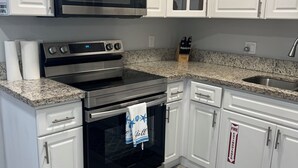 Una cocina con armarios blancos, electrodomésticos de acero inoxidable, encimera de granito y señal de salida de incendios.