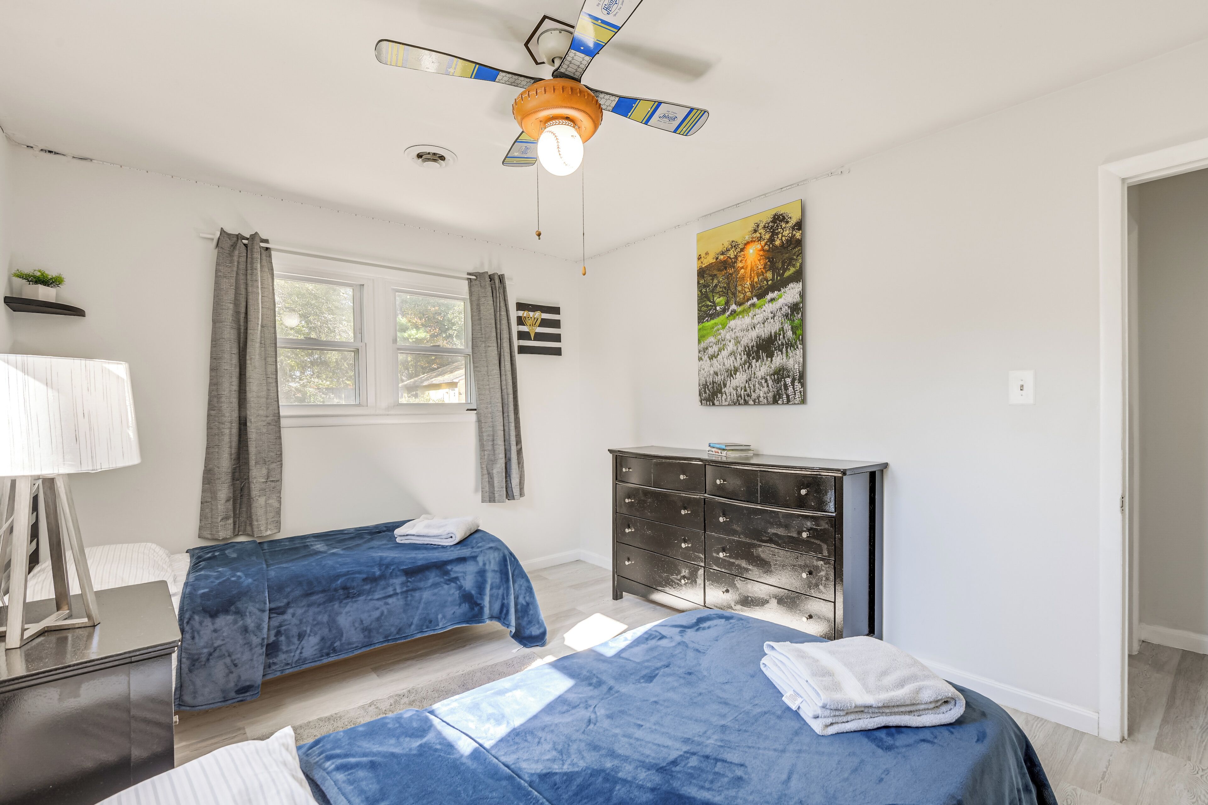 Un dormitorio con dos camas, un ventilador de techo, un aparador y una ventana con cortinas.