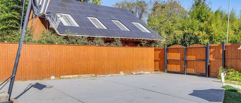 Quintal com cesta de basquete, cerca de madeira e casa com painéis solares.
