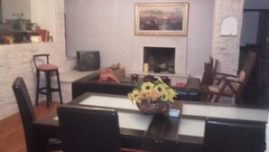 Ένα σαλόνι με τζάκι, τηλεόραση και τραπεζαρία με τραπέζι και καρέκλες.