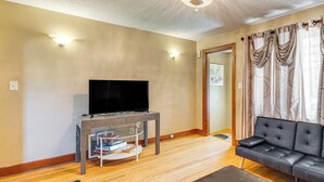 A living room with a flat-screen TV on a table, a leather sofa, and a wooden floor. - Large Yard Deck 20 Min to Highmark Stadium (Buffalo)