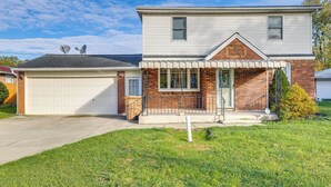 Ein zweistöckiges Haus mit Garage, Ziegelaußenwand und kleiner Veranda.