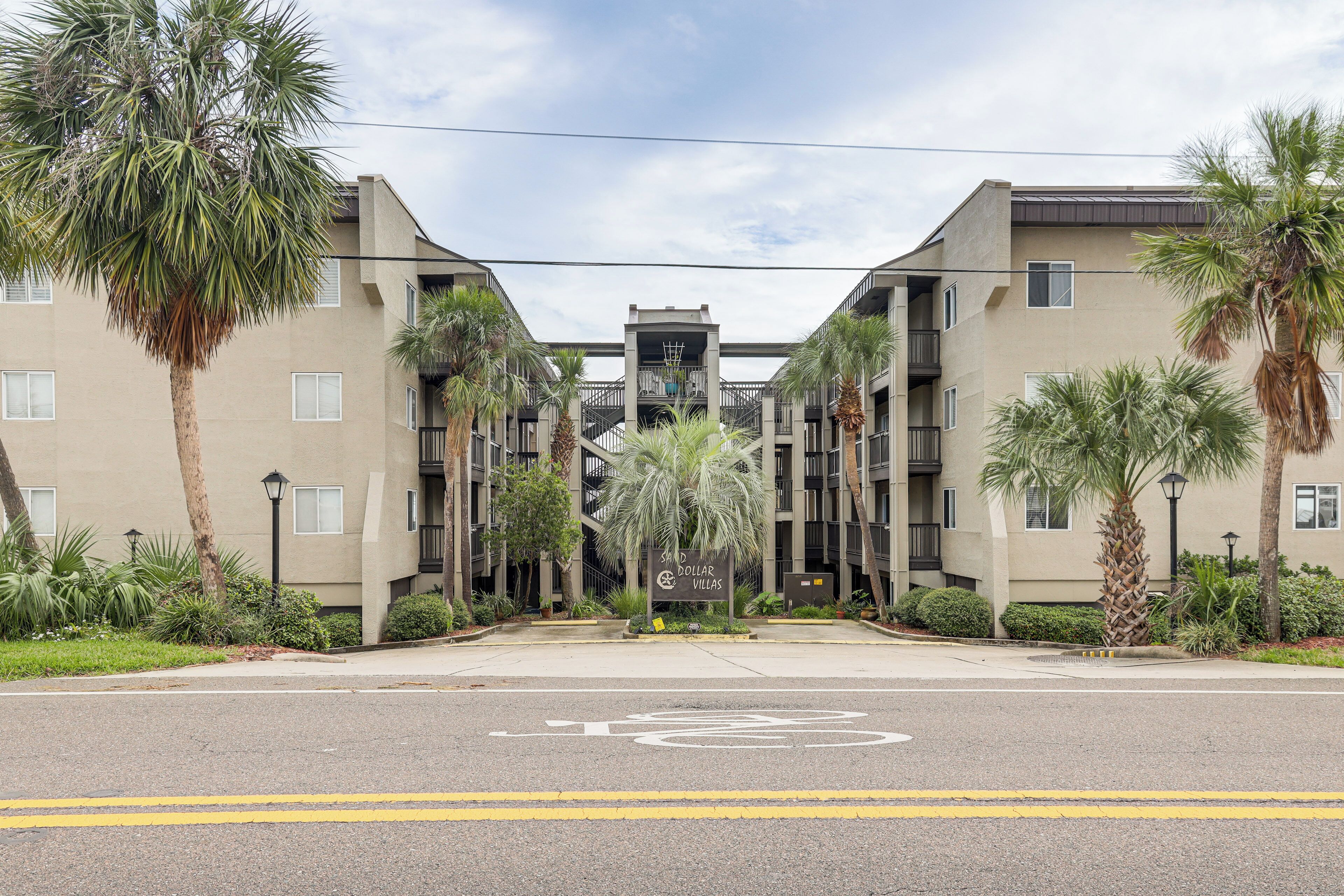 A multi-story building with a central entrance, surrounded by palm trees and a bicycle lane.