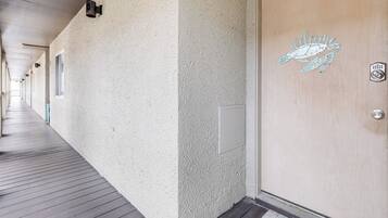 A corridor with a wooden deck, a textured wall, and a door with a 'welcome' sign.