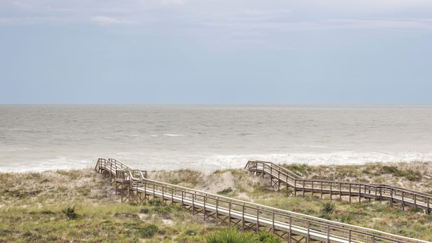 Een houten looppad dat naar een strand leidt, met de oceaan op de achtergrond.