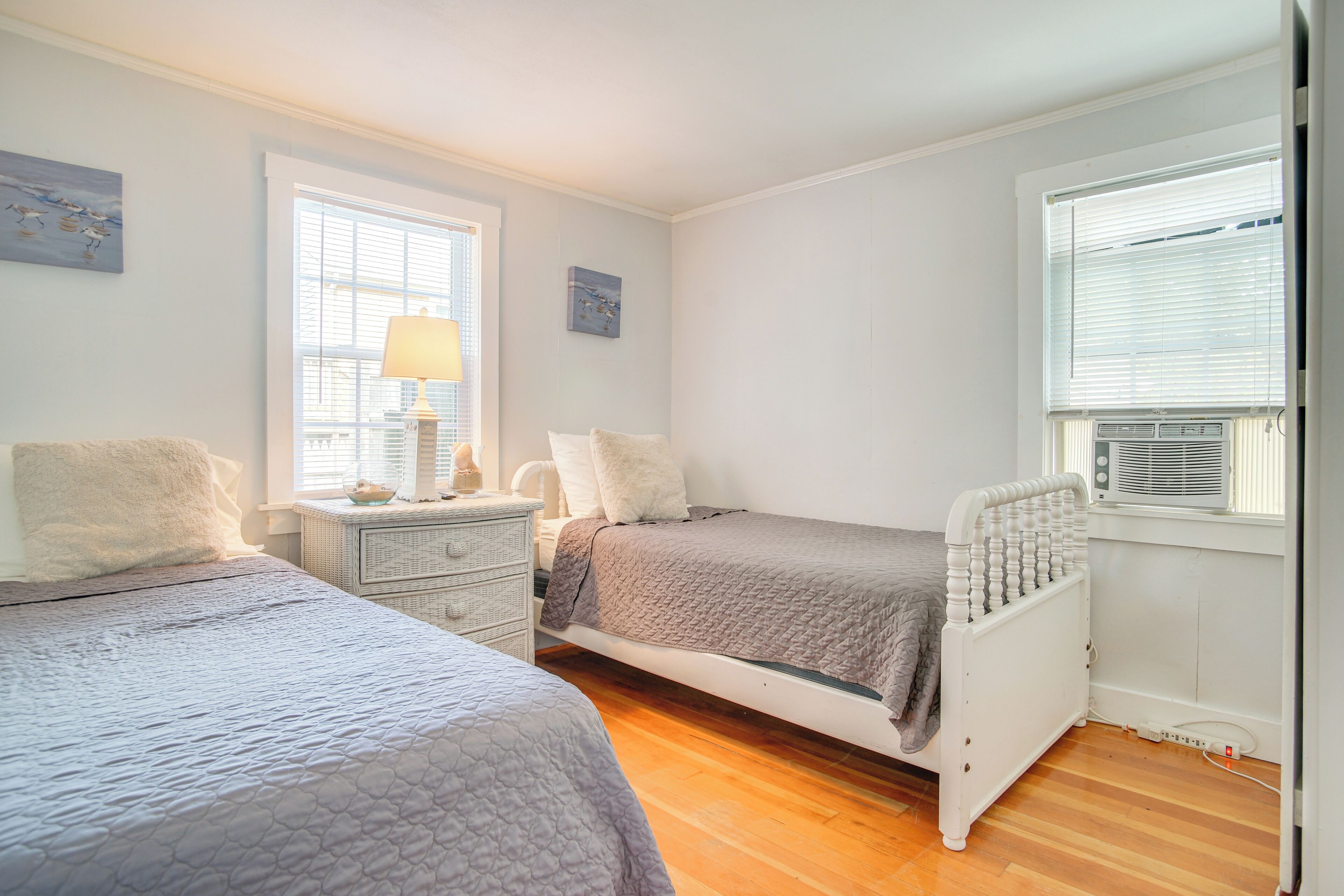 A bedroom with two beds, a nightstand, a lamp, and a window with blinds.