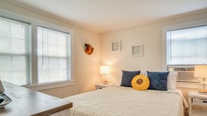 A bedroom with a bed, two bedside tables, a lamp, and a wall-mounted heater. - Walk to Beaches & Dining: Classic Cape Cod Cottage (Dennis Port)