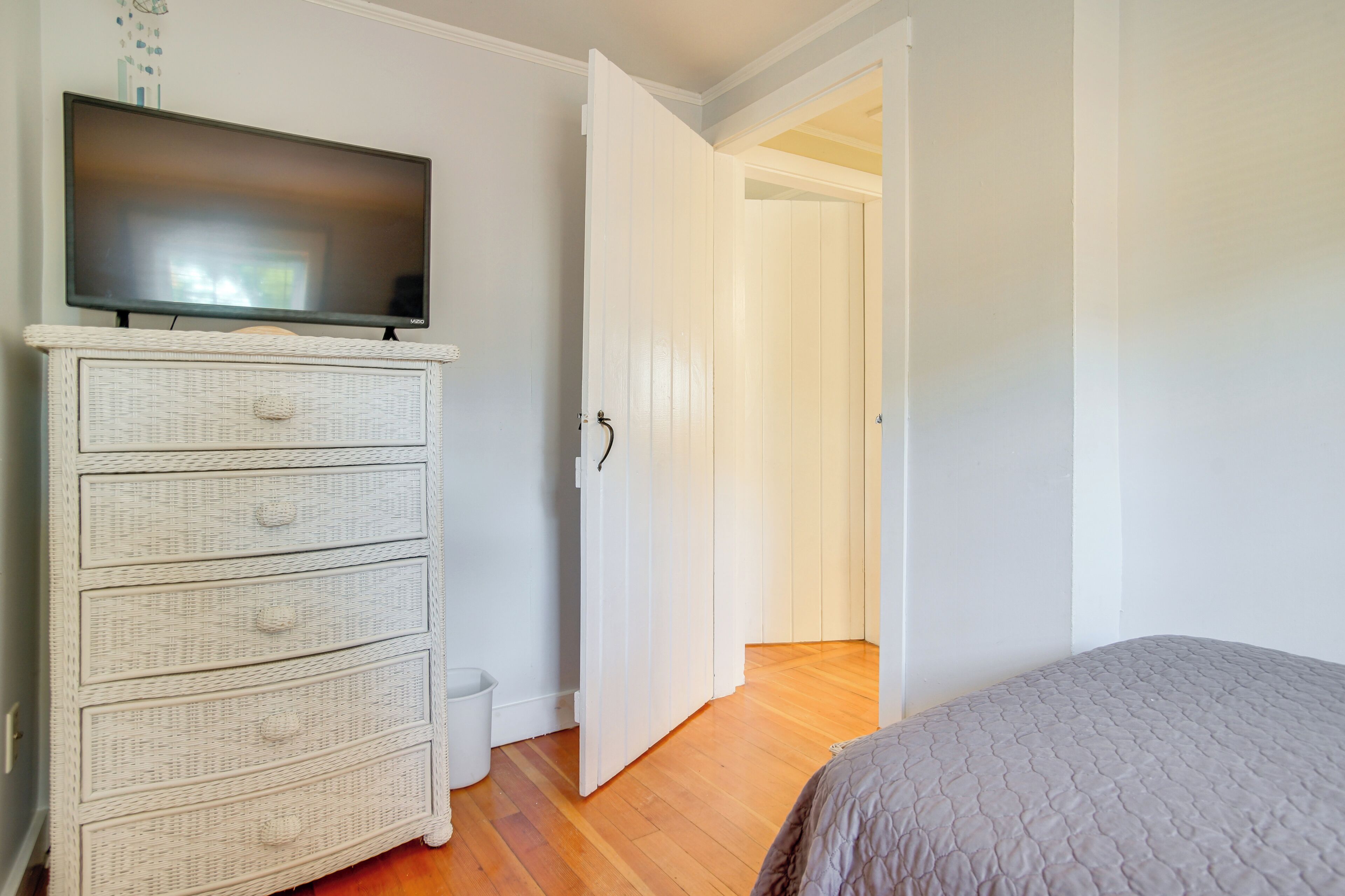 A bedroom with a bed, a television on a dresser, and a door leading to another room.