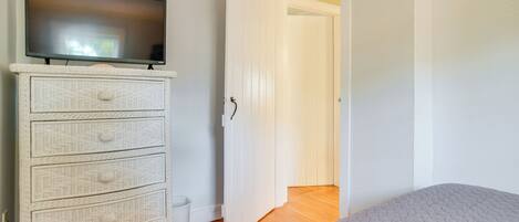 A bedroom with a bed, a television on a dresser, and a door leading to another room.