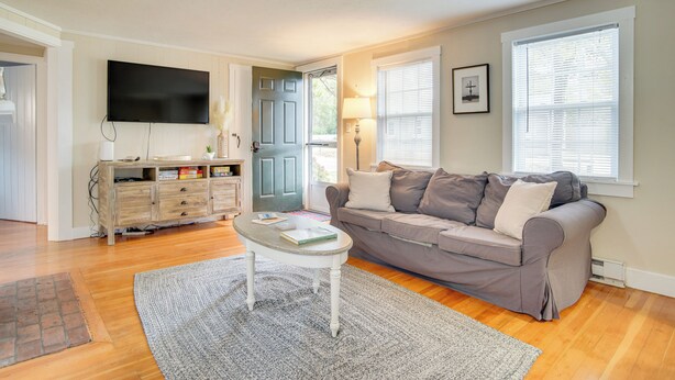 A living room with a grey sofa, a coffee table, a flat-screen TV, and a wooden cabinet. - Walk to Beaches & Dining: Classic Cape Cod Cottage (Dennis Port)