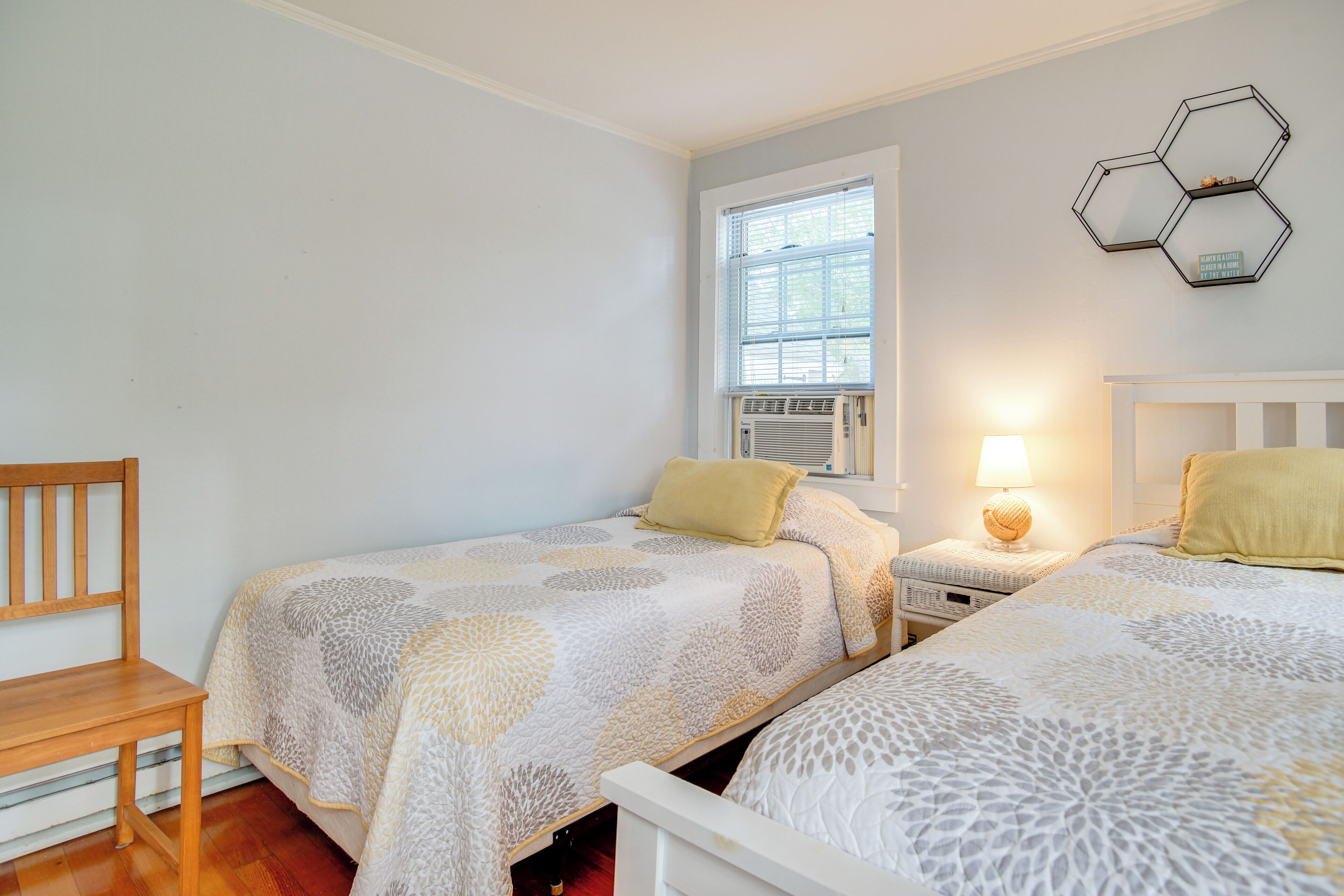 Une chambre avec deux lits, une chaise en bois, une fenêtre et un luminaire hexagonal fixé au mur.