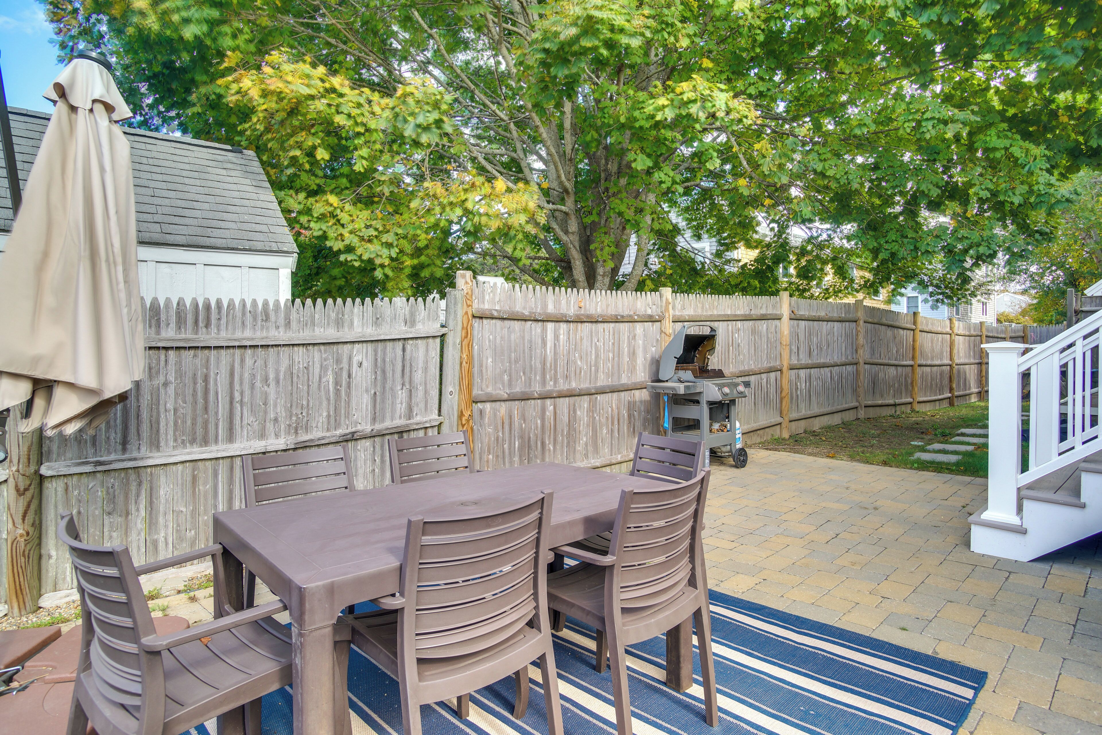 A patio with a table and chairs, a barbecue grill, and a wooden fence.
